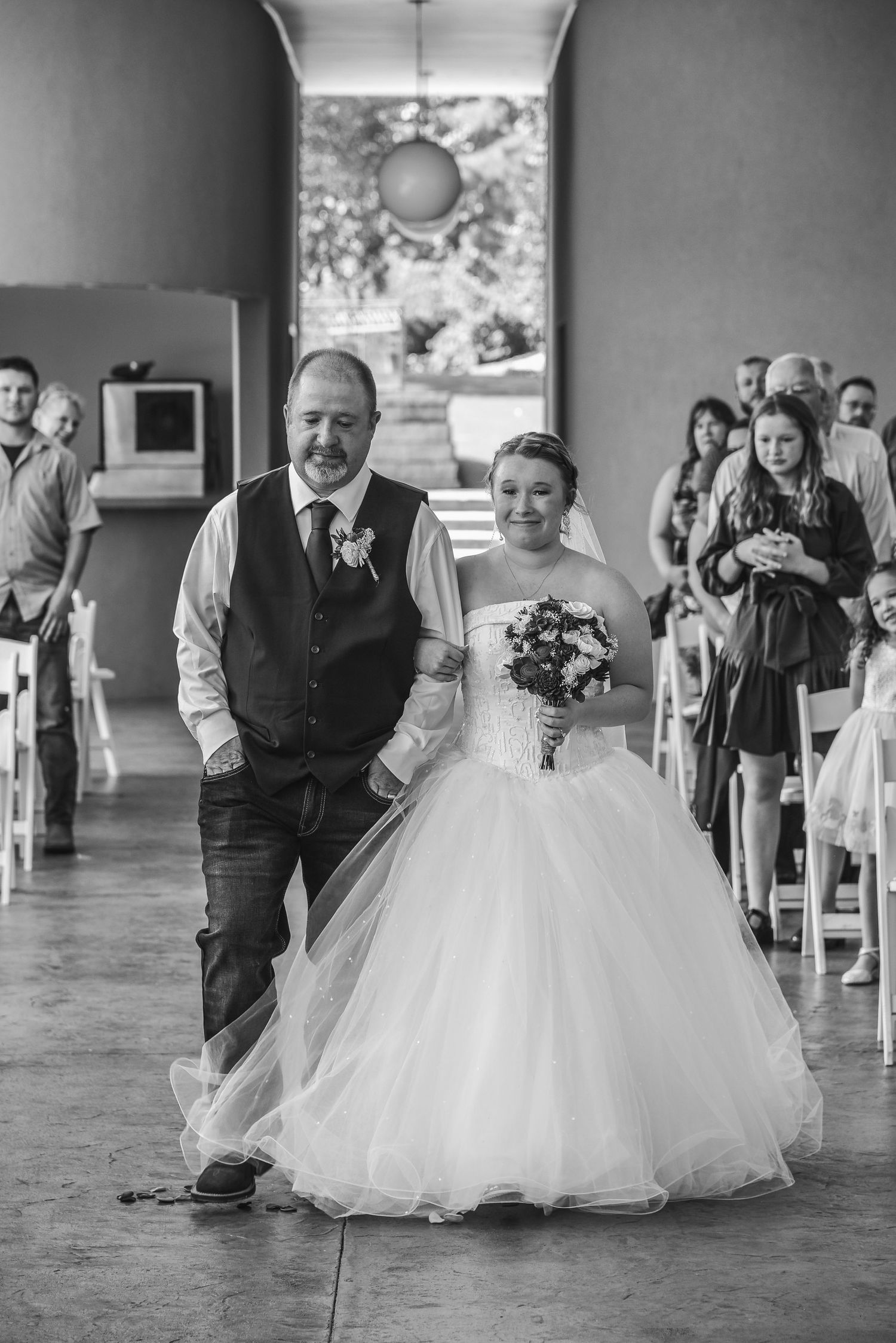 A traditional wedding ceremony processional in a rustic indoor venue with natural light streaming through windows.