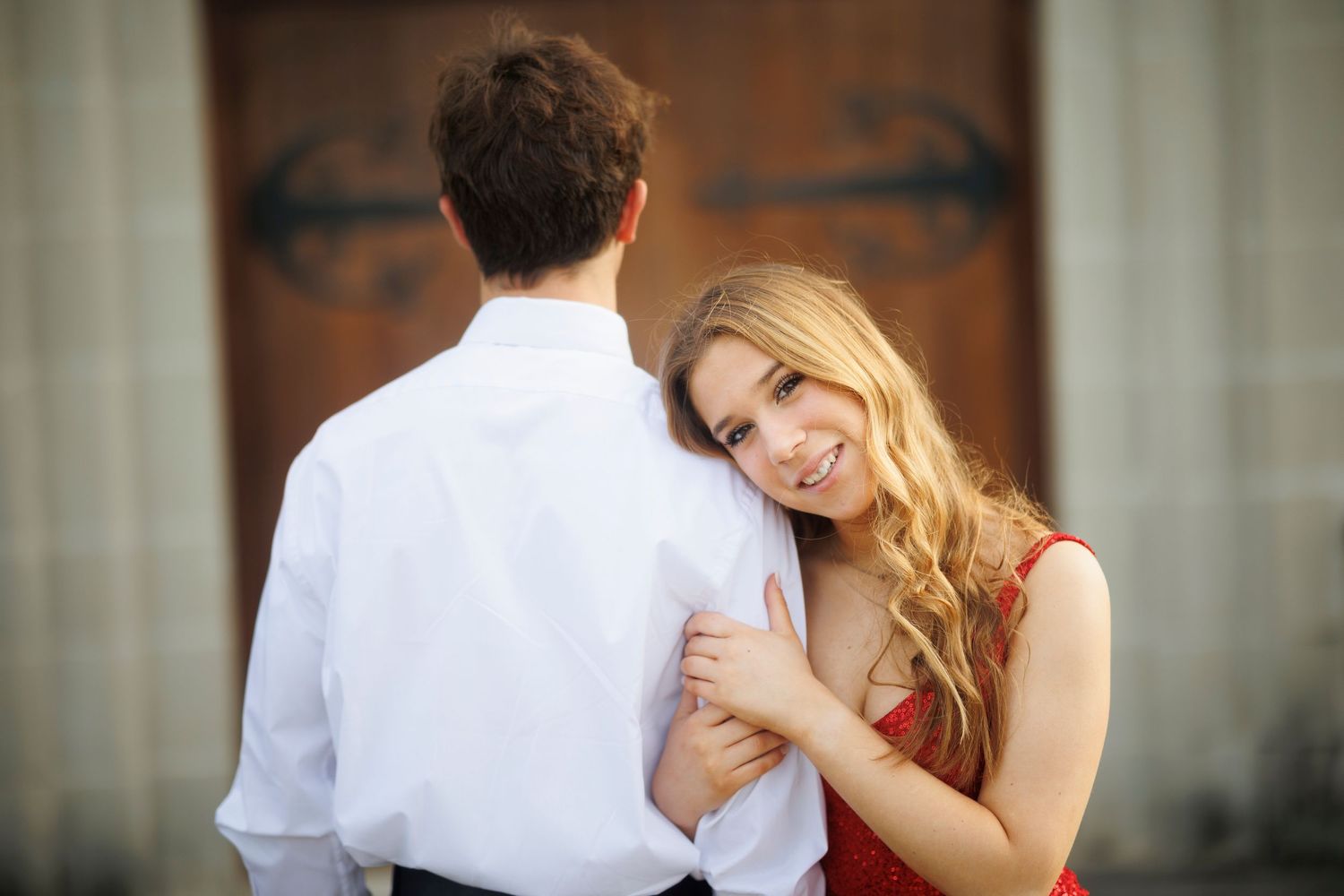 Romantic couple embracing in formal attire against wooden door background.