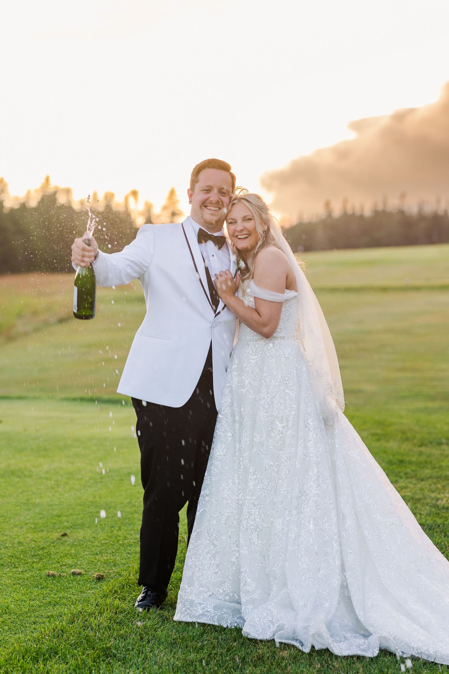 A joyful wedding celebration with champagne spraying in a sunlit outdoor field.