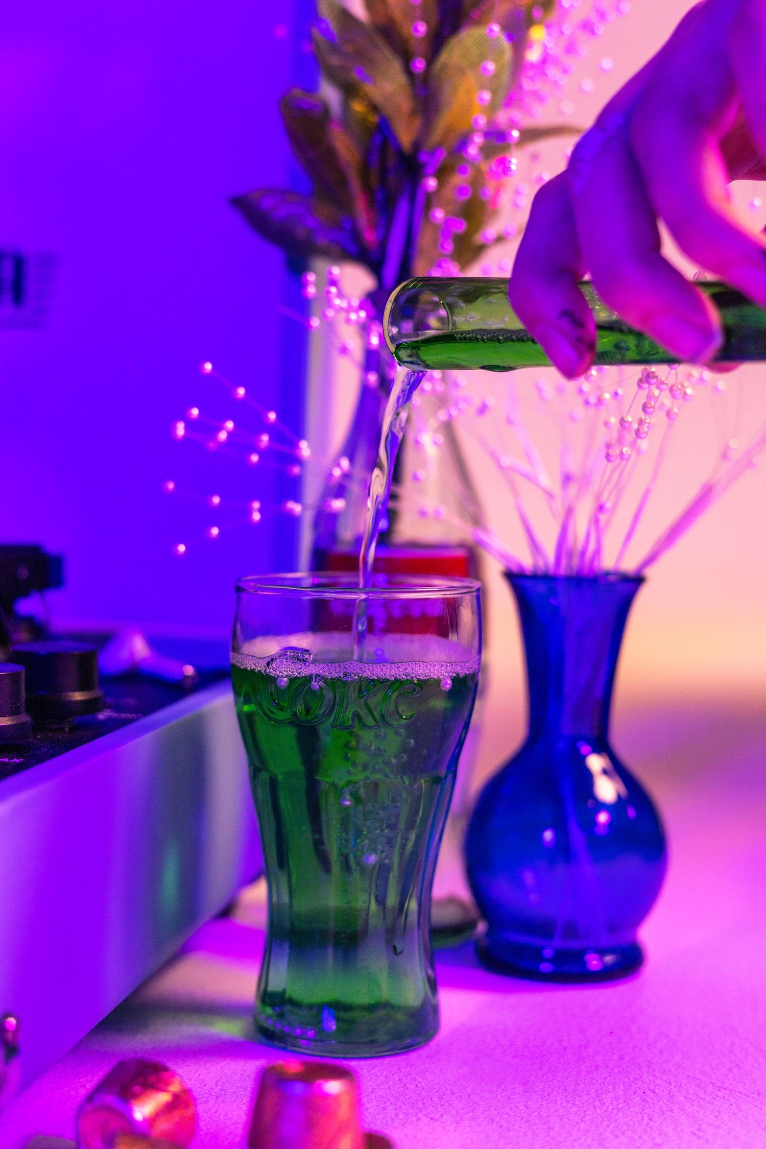 Green liquid being poured into glass with purple atmospheric lighting.