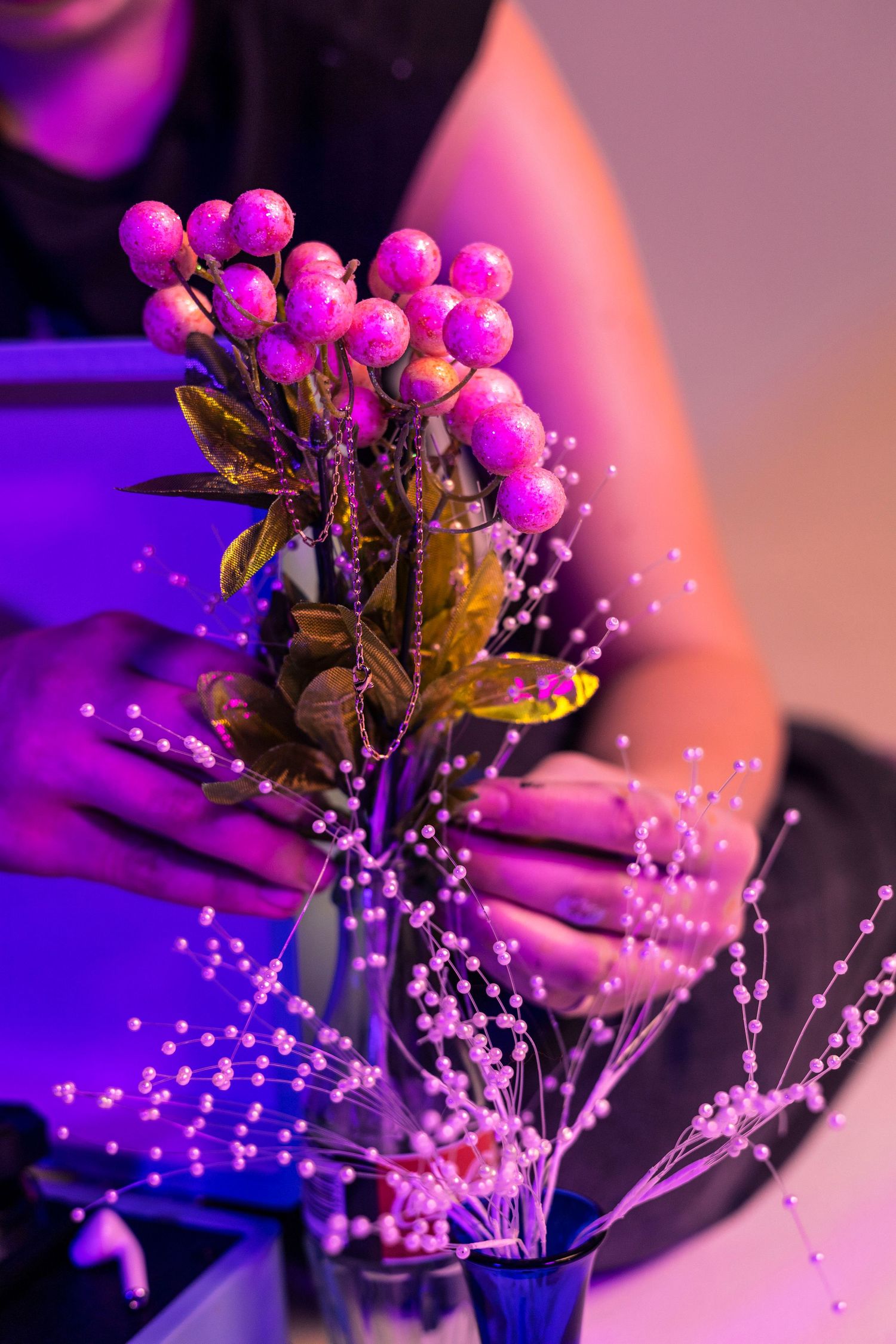 Pink berries and delicate flowers bathed in purple lighting create a dreamy botanical arrangement.