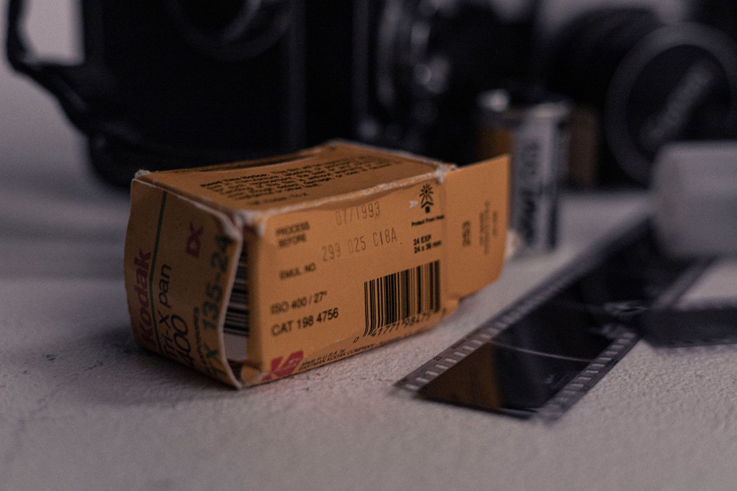 A vintage film box rests on a gray surface next to photography equipment.