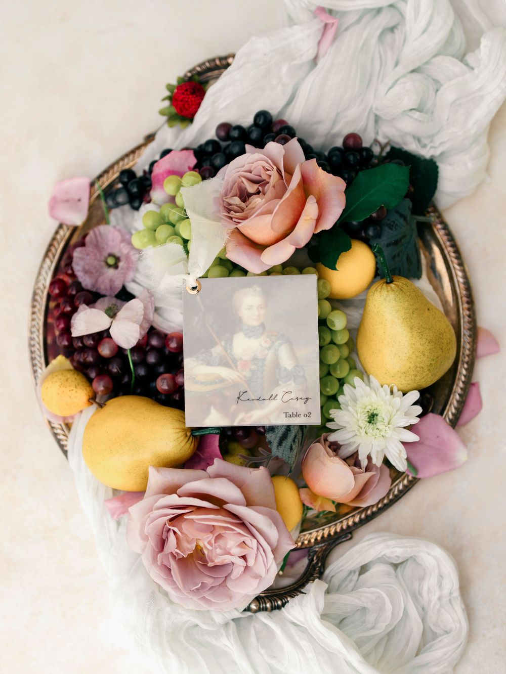 Elegant silver tray with fresh fruit, roses, and vintage photographs arranged artistically.