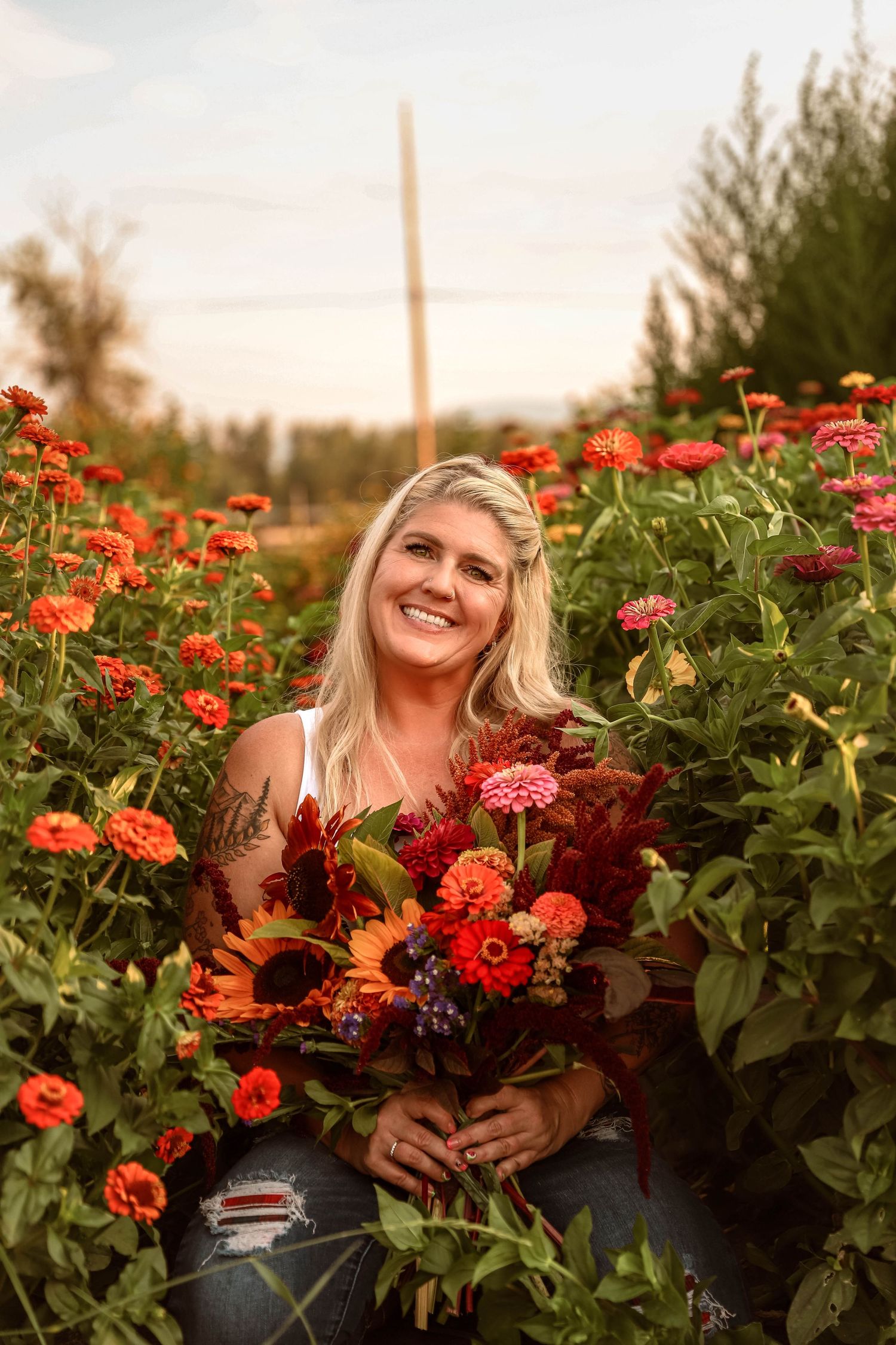 Portrait session in flower garden with subject holding vibrant fall bouquet at sunset.