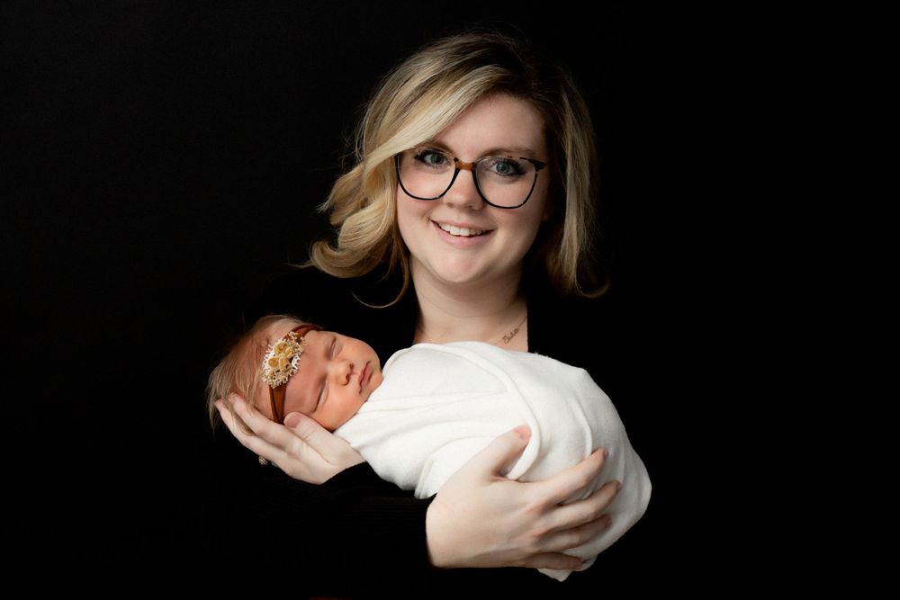 Studio portrait against black backdrop showing gentle parent-baby bonding moment.