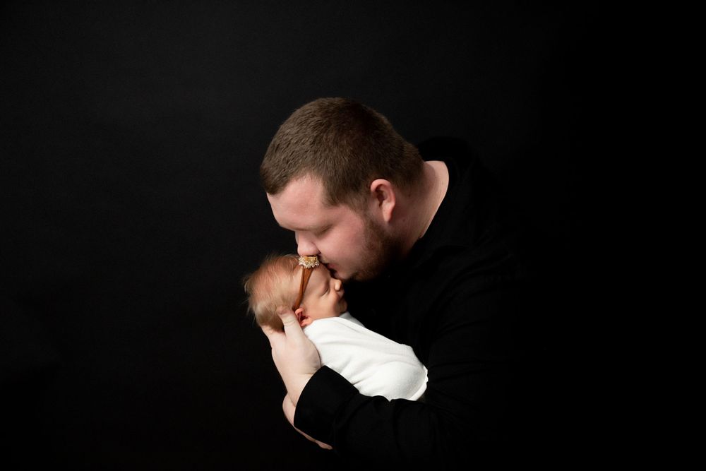 An intimate black and white portrait showing tender parent-child moment against dark background.