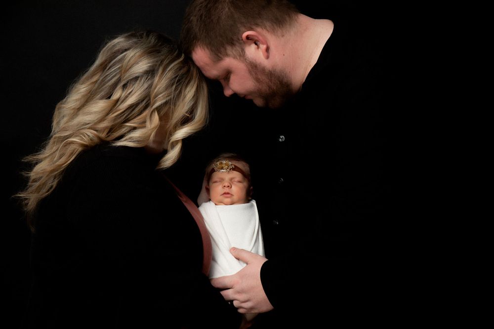 Artistic family portrait with dramatic lighting showing parents embracing infant.