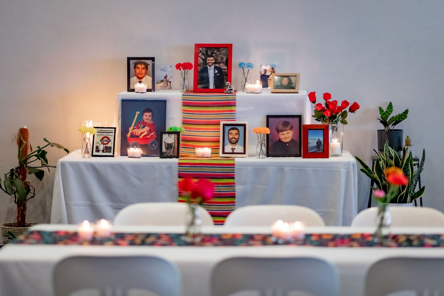 A memorial table display with photo frames, flowers and candles on a white tablecloth.