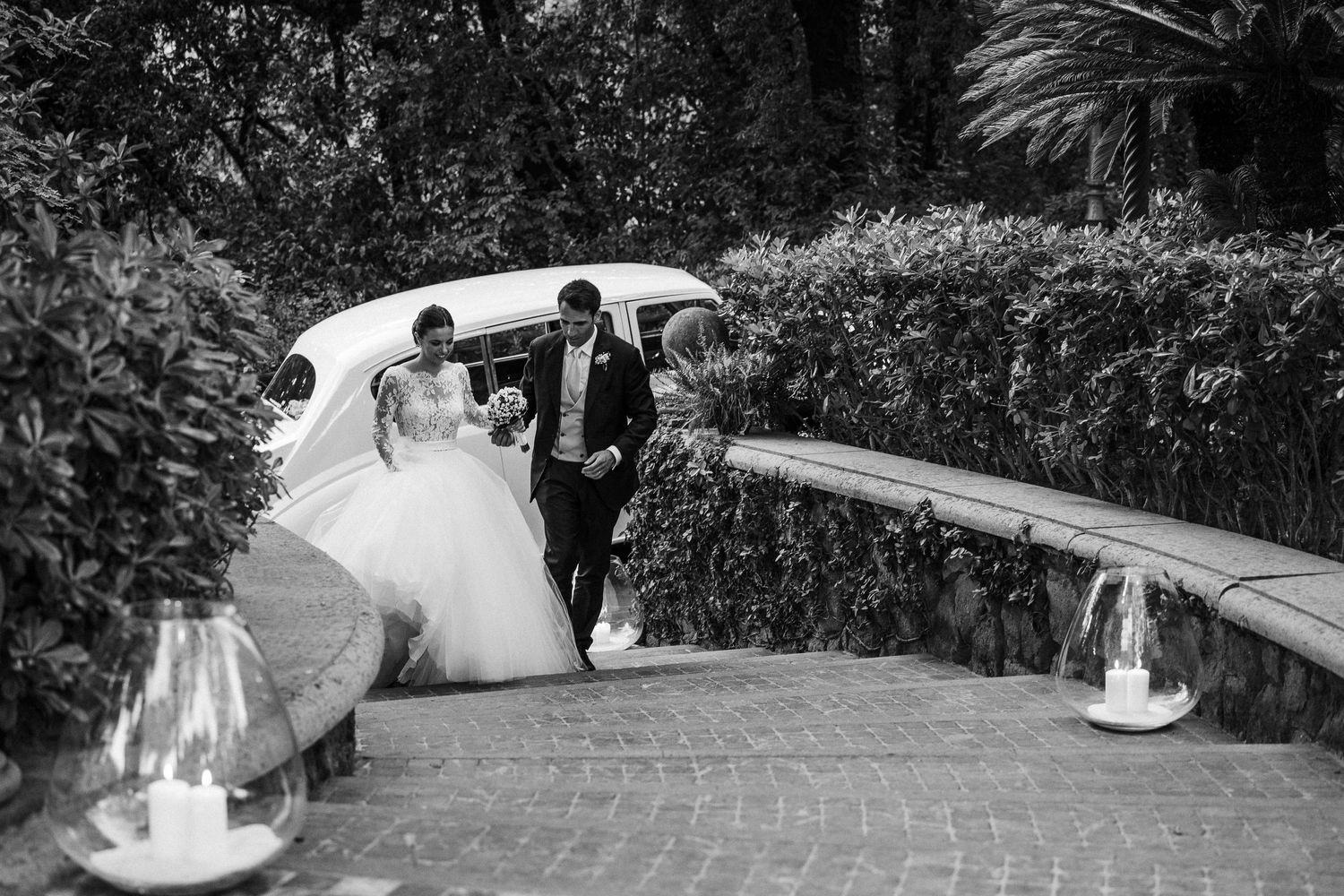 A couple walks down a garden path adorned with lanterns during their wedding celebration.