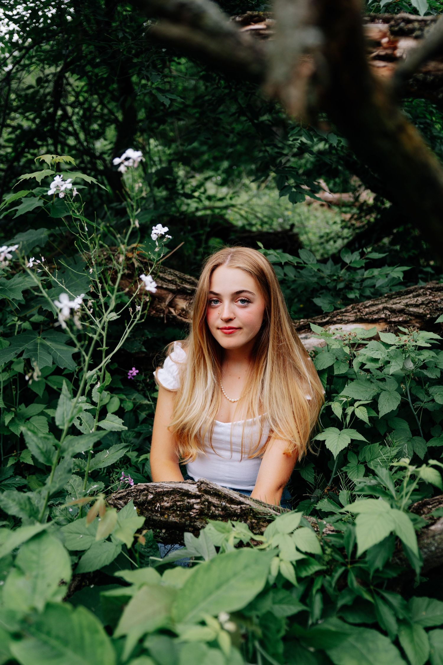 A nature portrait showing someone amongst wildflowers and tree branches in a whimsical forest setting.
