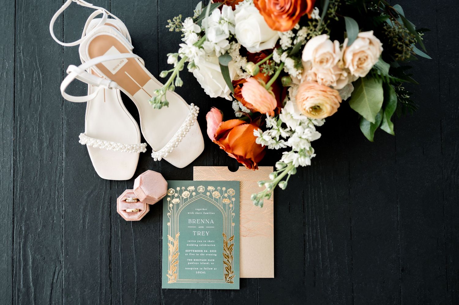 Wedding details featuring peach and orange roses with invitation suite on dark background.