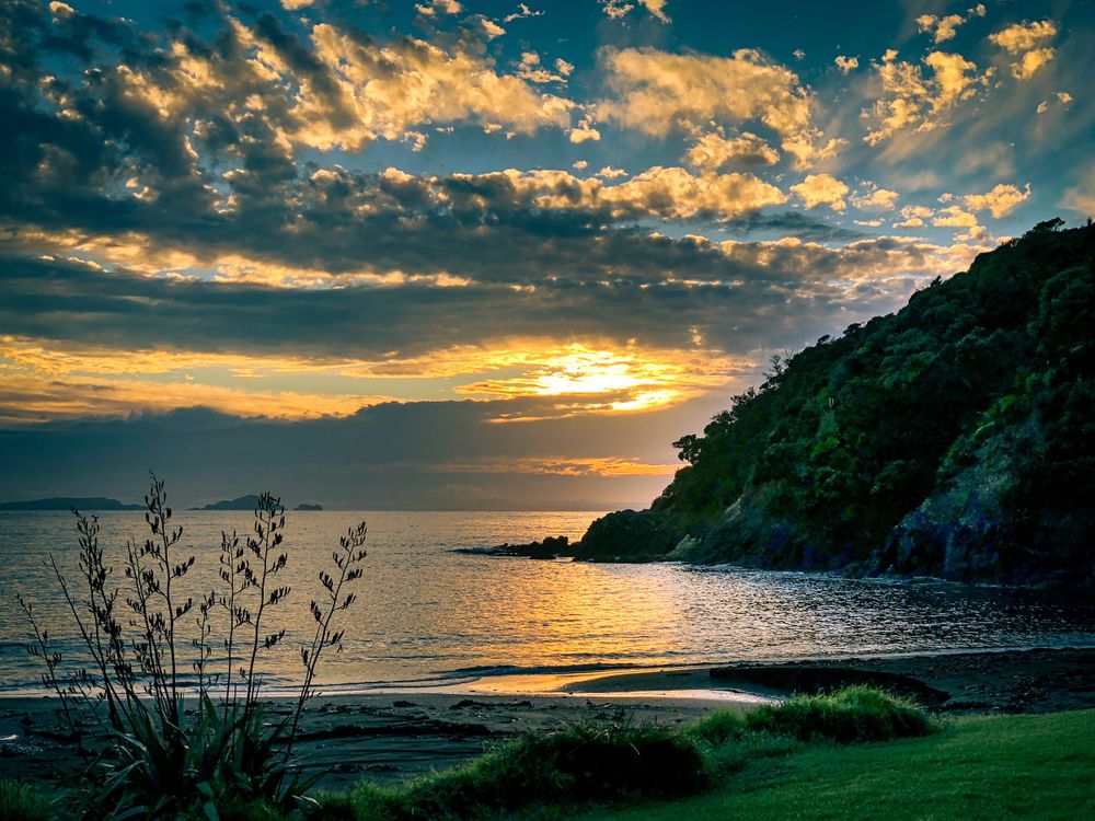 Dramatic sunset clouds paint the sky in golden hues over a tranquil coastal landscape.