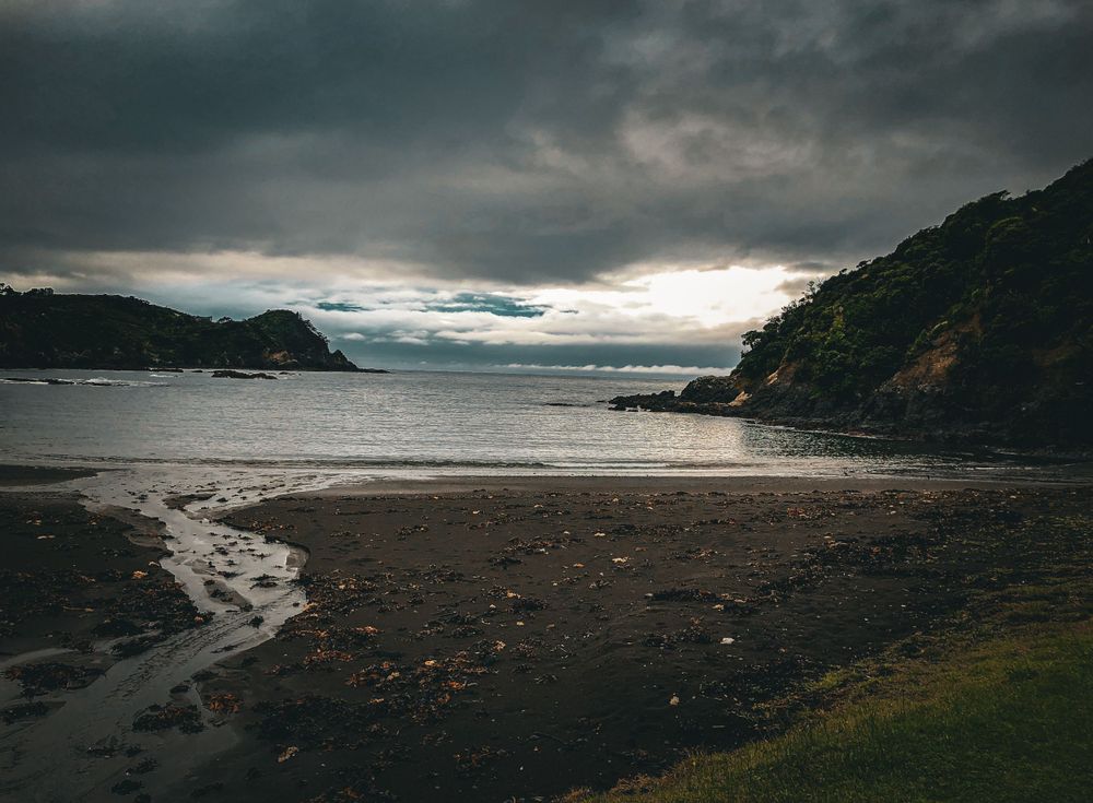 Misty coastal landscape with dark storm clouds rolling over rocky beach at sunset.
