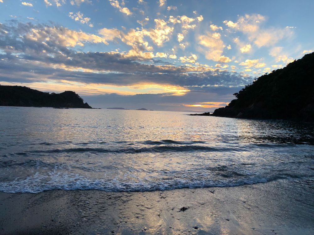 Serene coastal sunset with gentle waves rolling onto shore under pastel-colored clouds.