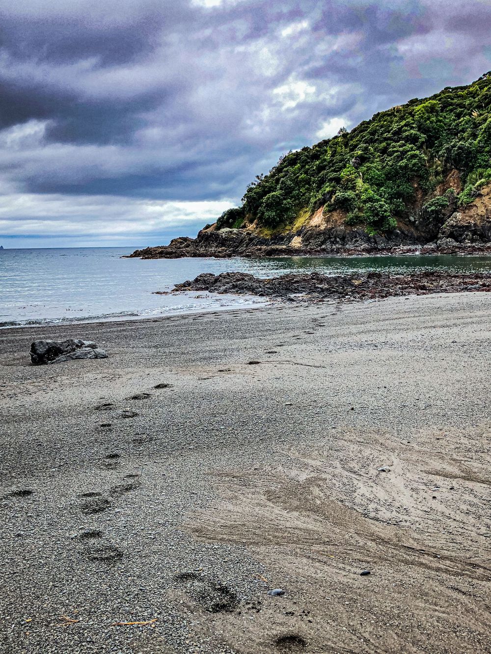 Grey pebble beach curves around a rocky headland under dramatic overcast skies.
