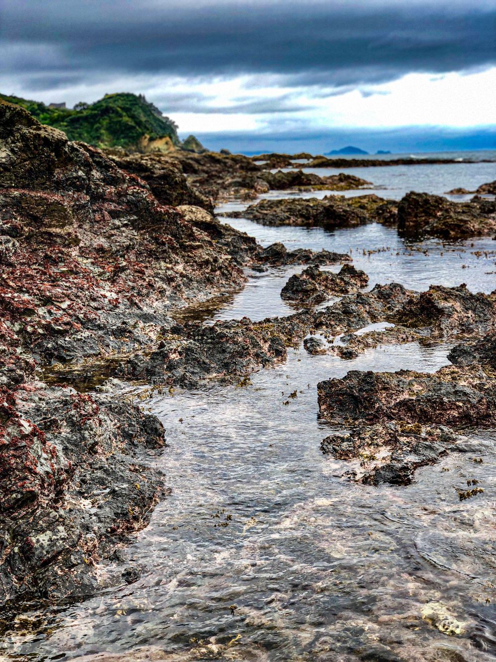 Rocky tidal pools and rugged coastal formations stretch along the shoreline under moody skies.