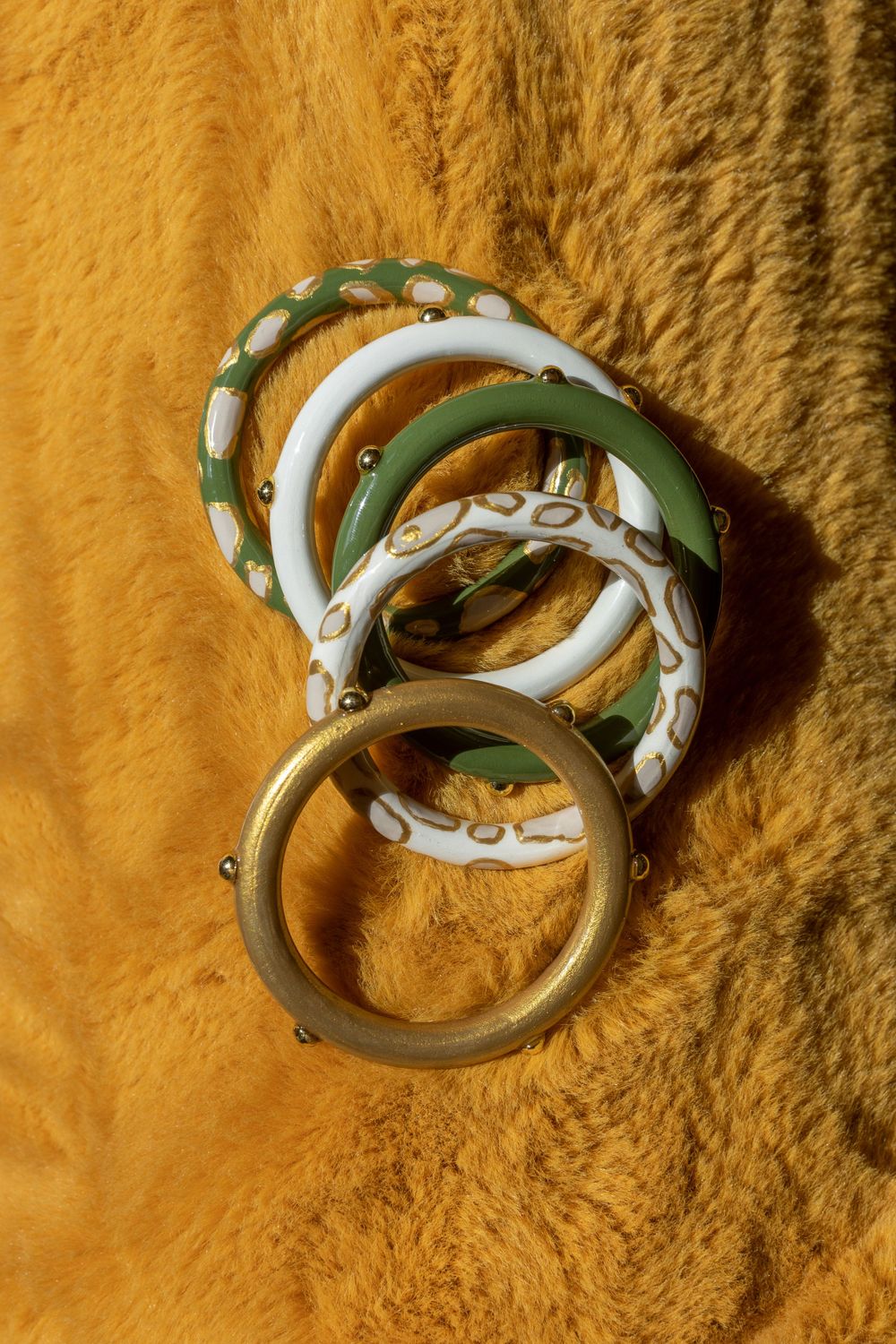 Decorative bangles in green and white patterns displayed on a golden textured background.