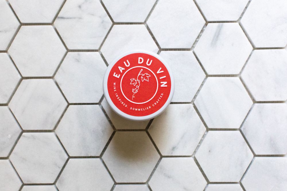 Red circular logo on white jar placed on hexagonal tile surface.