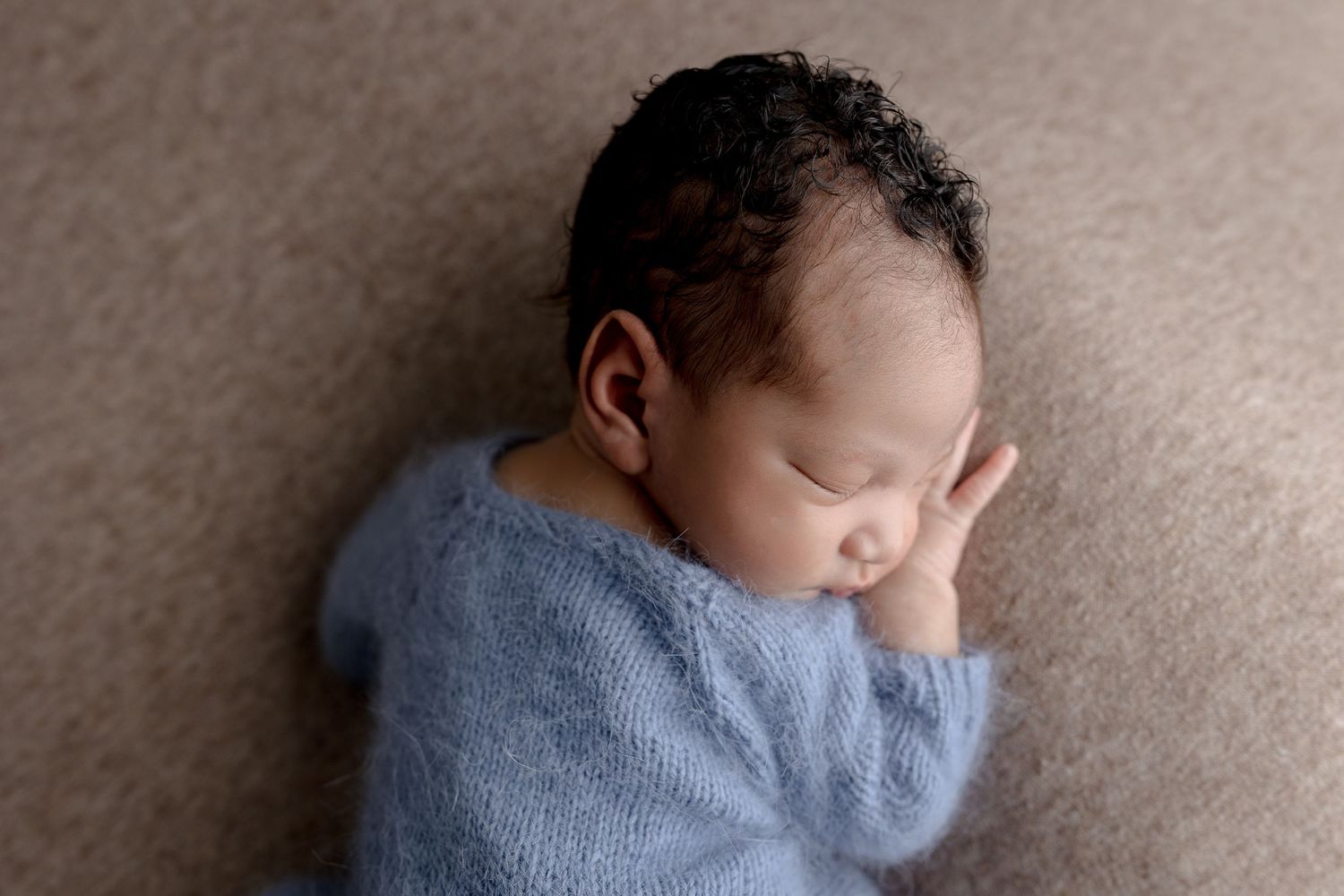 Sleeping newborn in soft blue sweater lying on neutral gray backdrop during professional photo session.