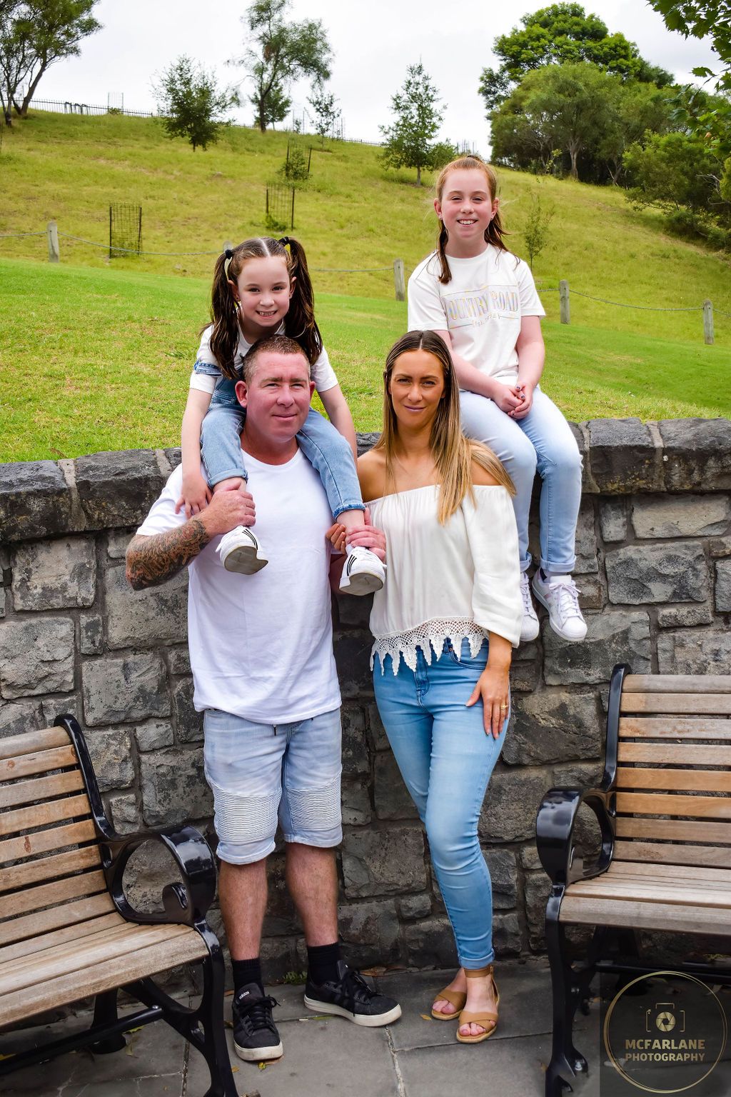 Family posing on stone wall with benches in outdoor setting.
