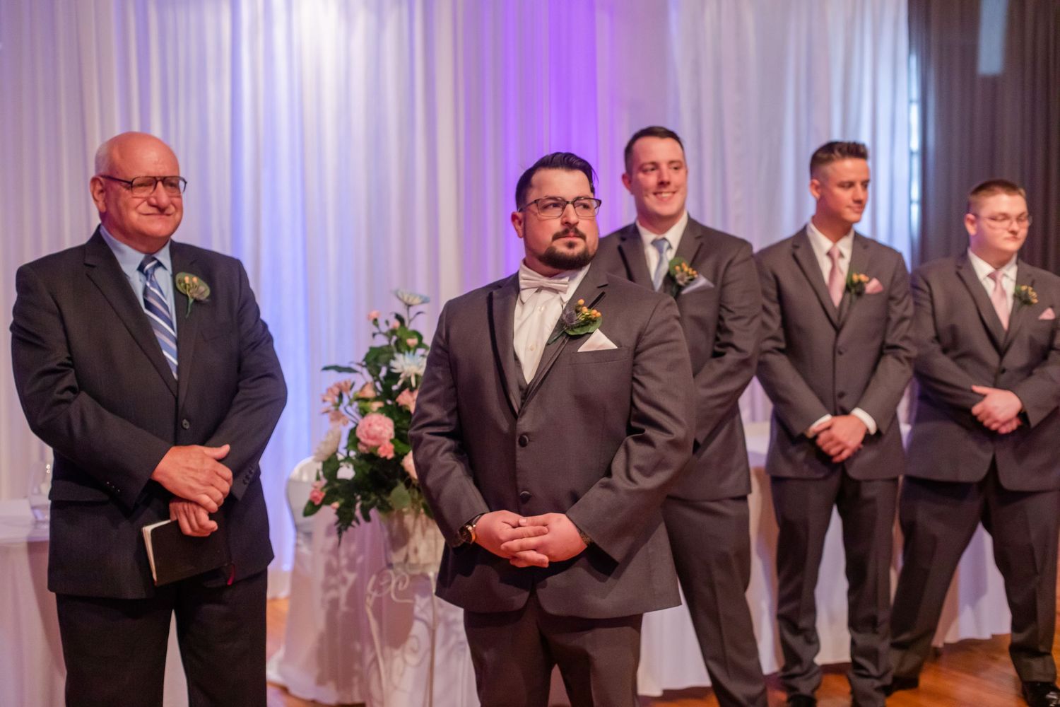 Formal wedding ceremony setup with groomsmen in dark suits standing in formation.