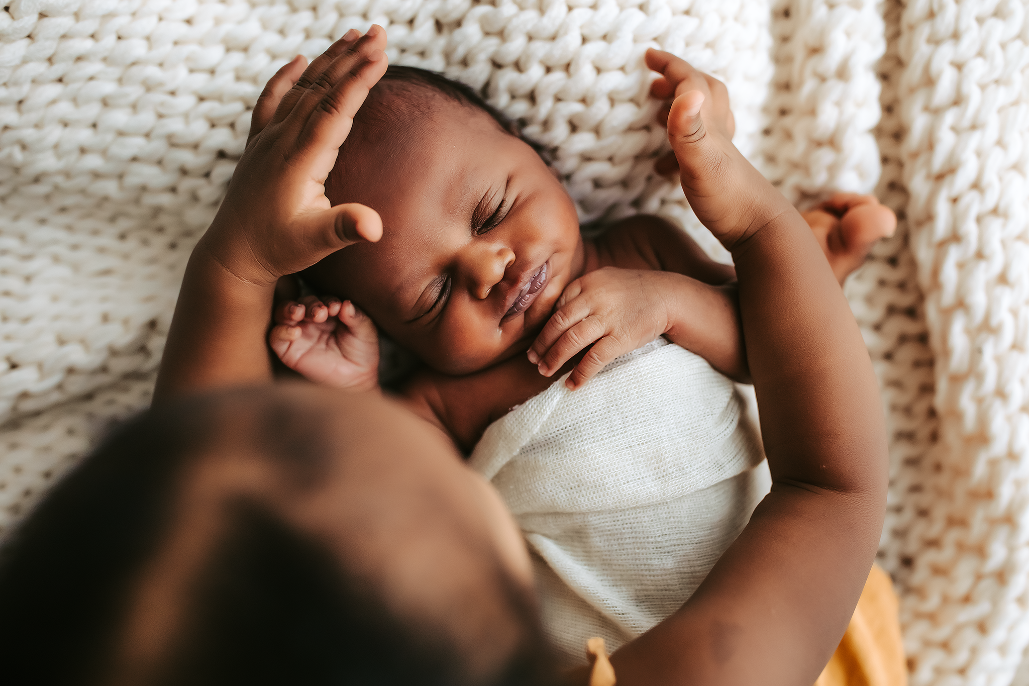 Sleeping newborn wrapped in white blanket lies on textured knit blanket with outstretched arms. Columbia, MO newborn photography studio