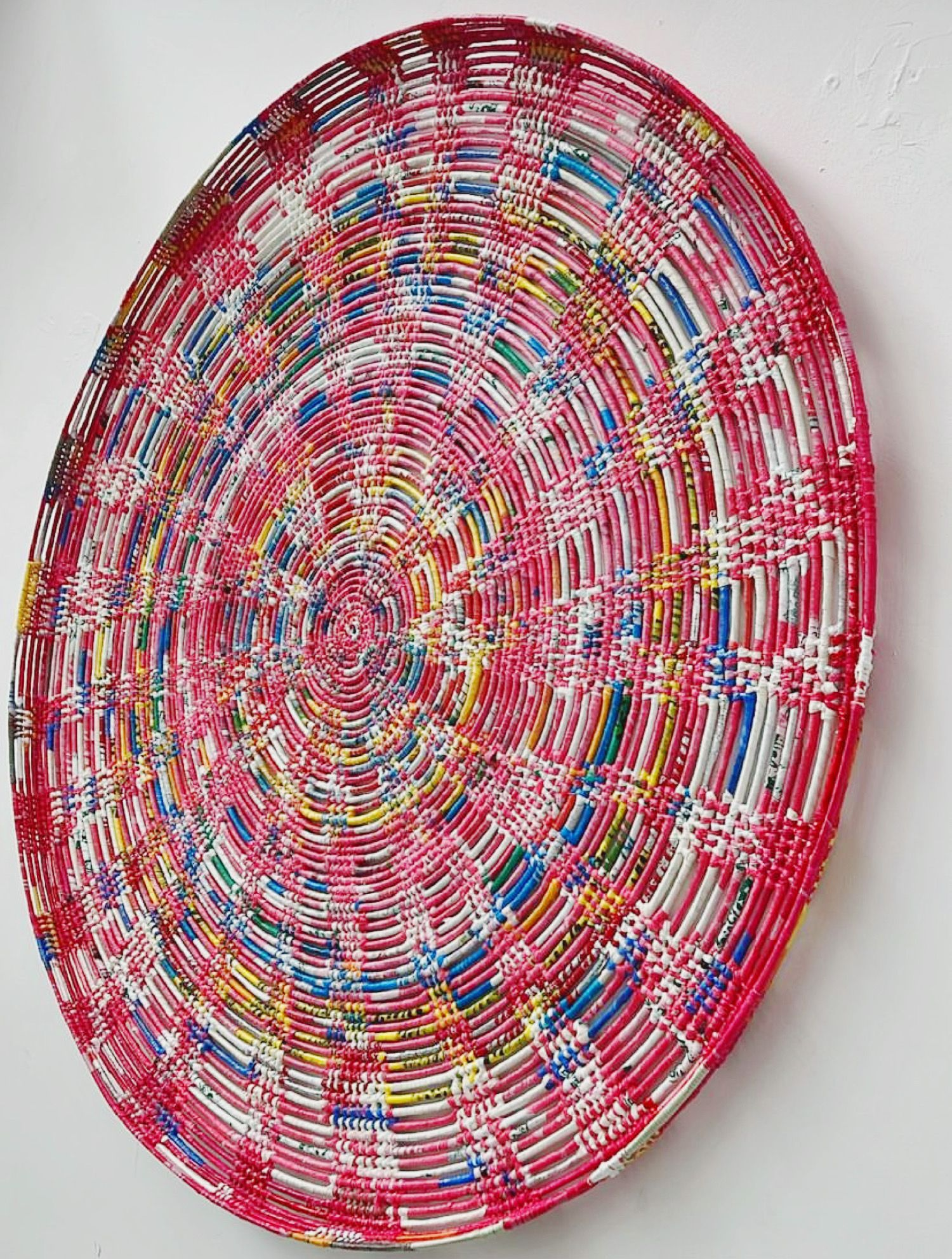 Circular woven textile art piece with concentric patterns in red and multicolored designs.