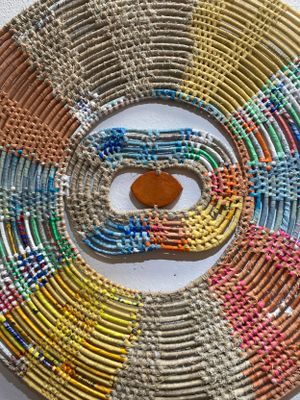 Close-up of circular beaded art piece showing intricate geometric patterns in earth tones and bright colors.
