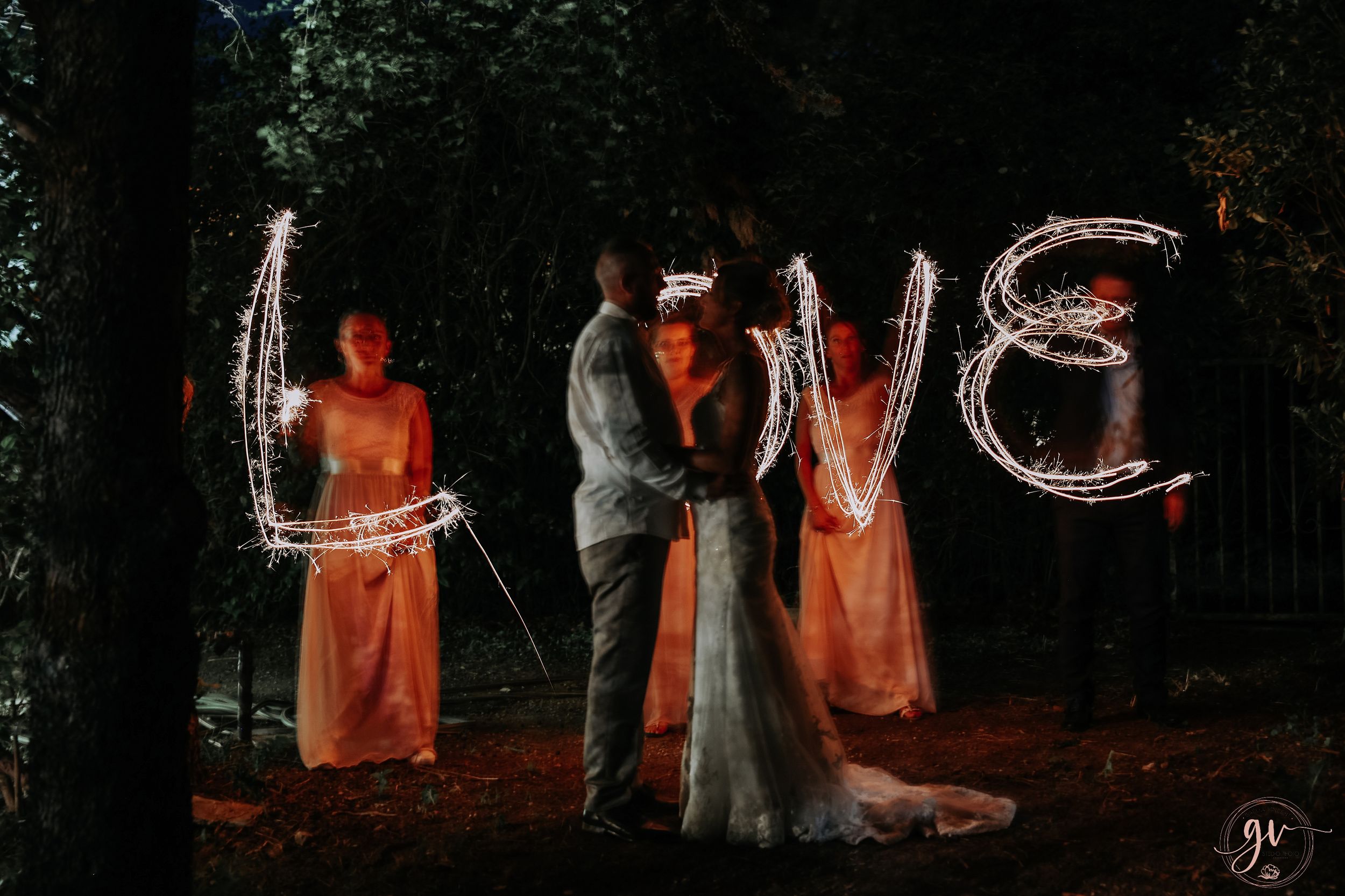 Creative nighttime wedding photo with light painting spelling 'LOVE' among dark trees.