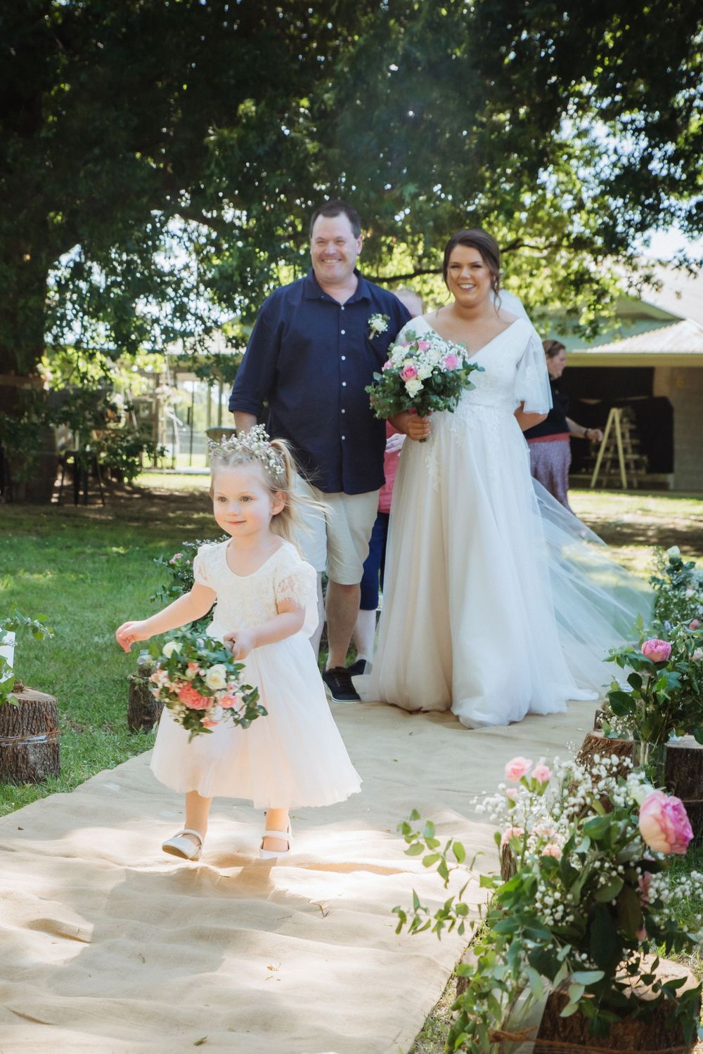 casually dressed father of bride walking brunette bride wearing blush dress down aisle as flowergirl runs ahead