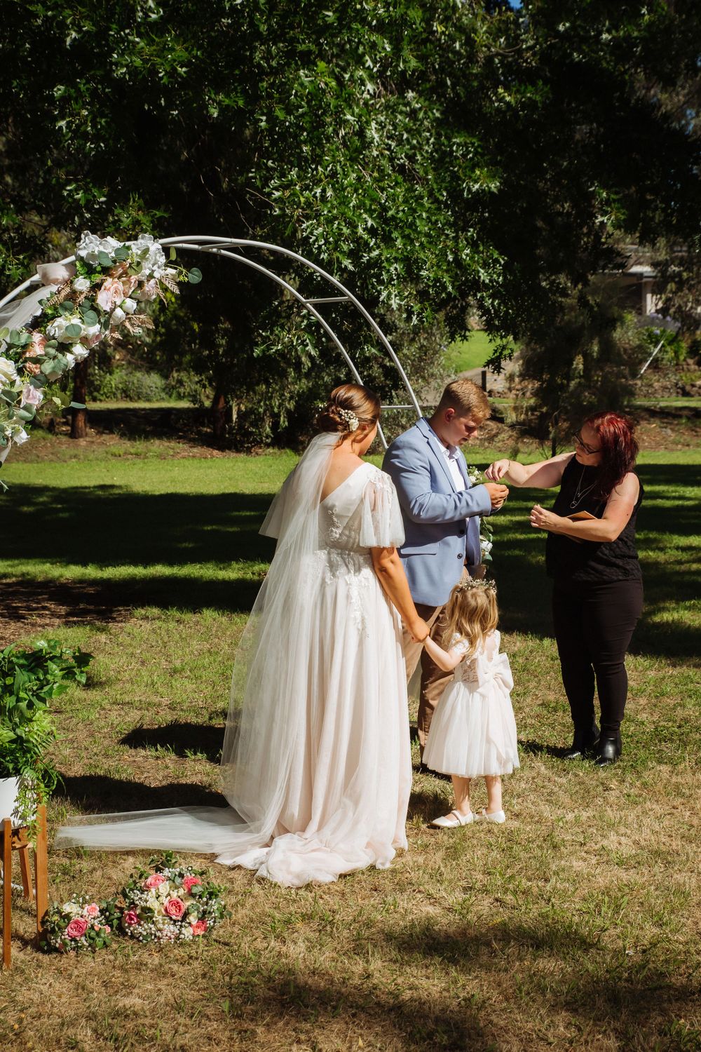 celebrant hands flowergirl gift to casually dressed groom as bride and daughter look on