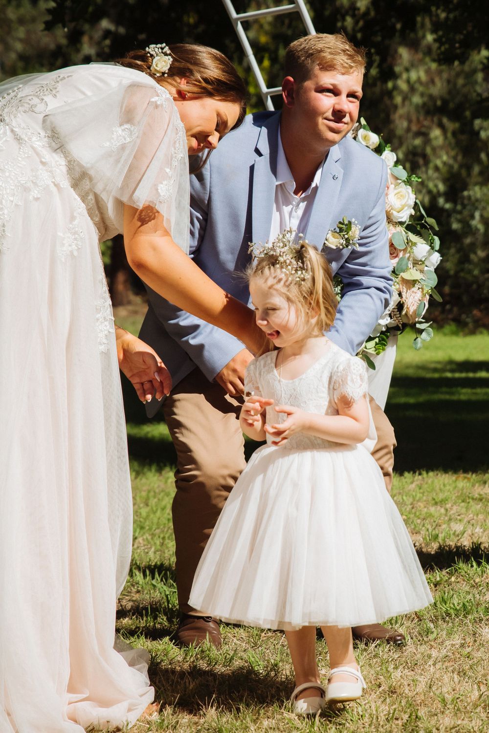 Sweet moment between couple and flower girl at outdoor garden wedding.
