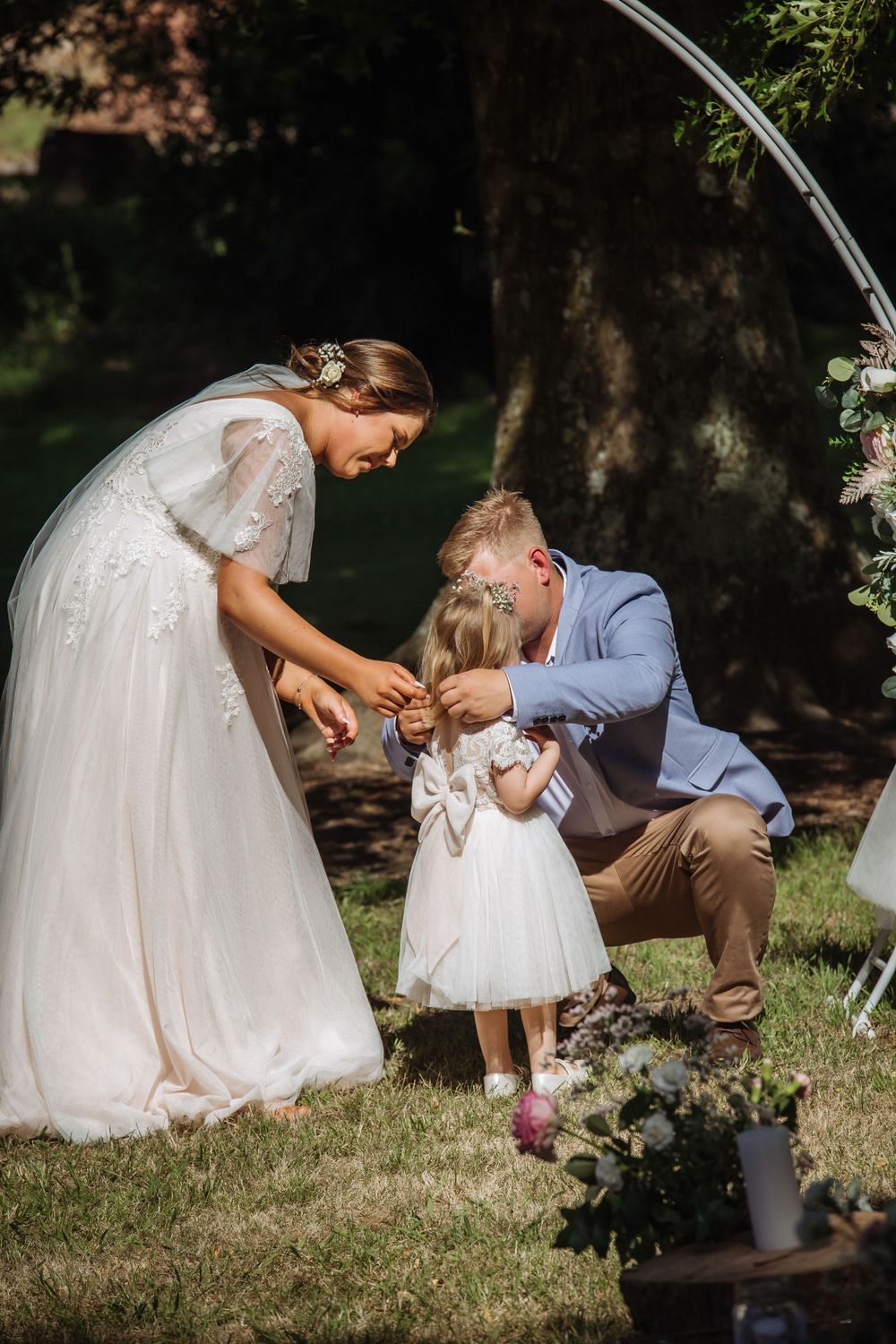 casually dressed groom in blue jacket places necklace on flowergirl in white as pregnant bride looks on