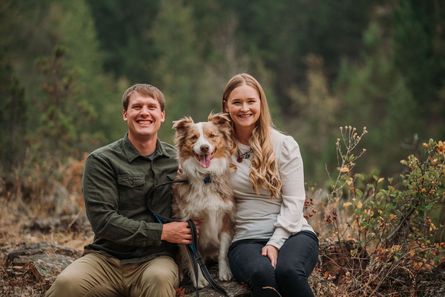 couple sitting on a rock with a dog between them
