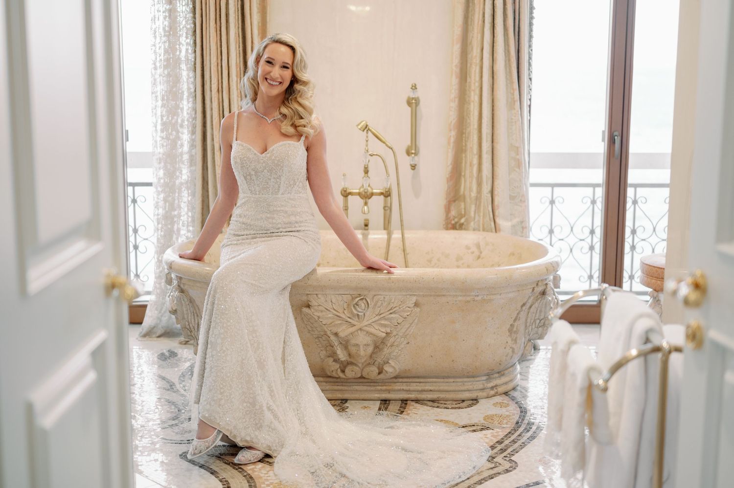 A bride in an elegant white wedding gown poses next to an ornate vintage bathtub.