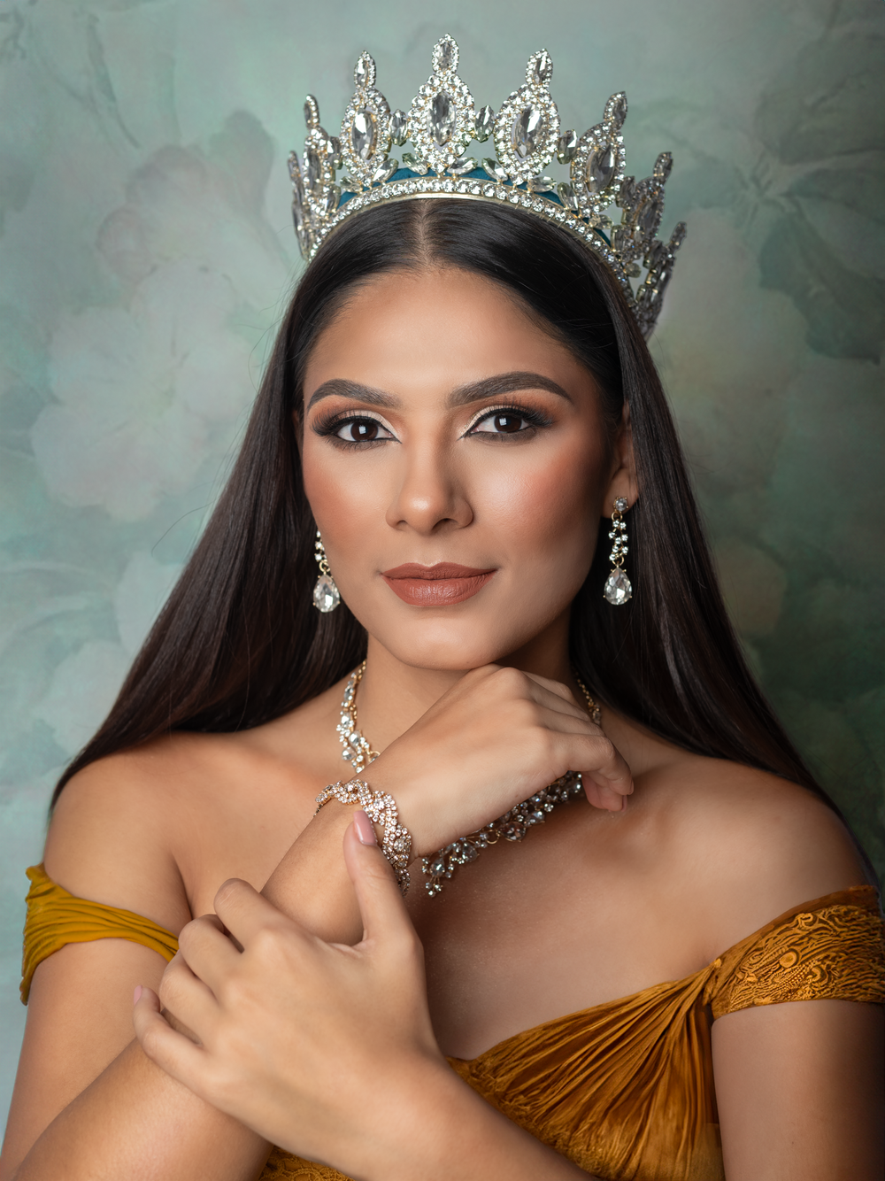 Beauty queen in gold off-shoulder dress wearing crystal crown and necklace.