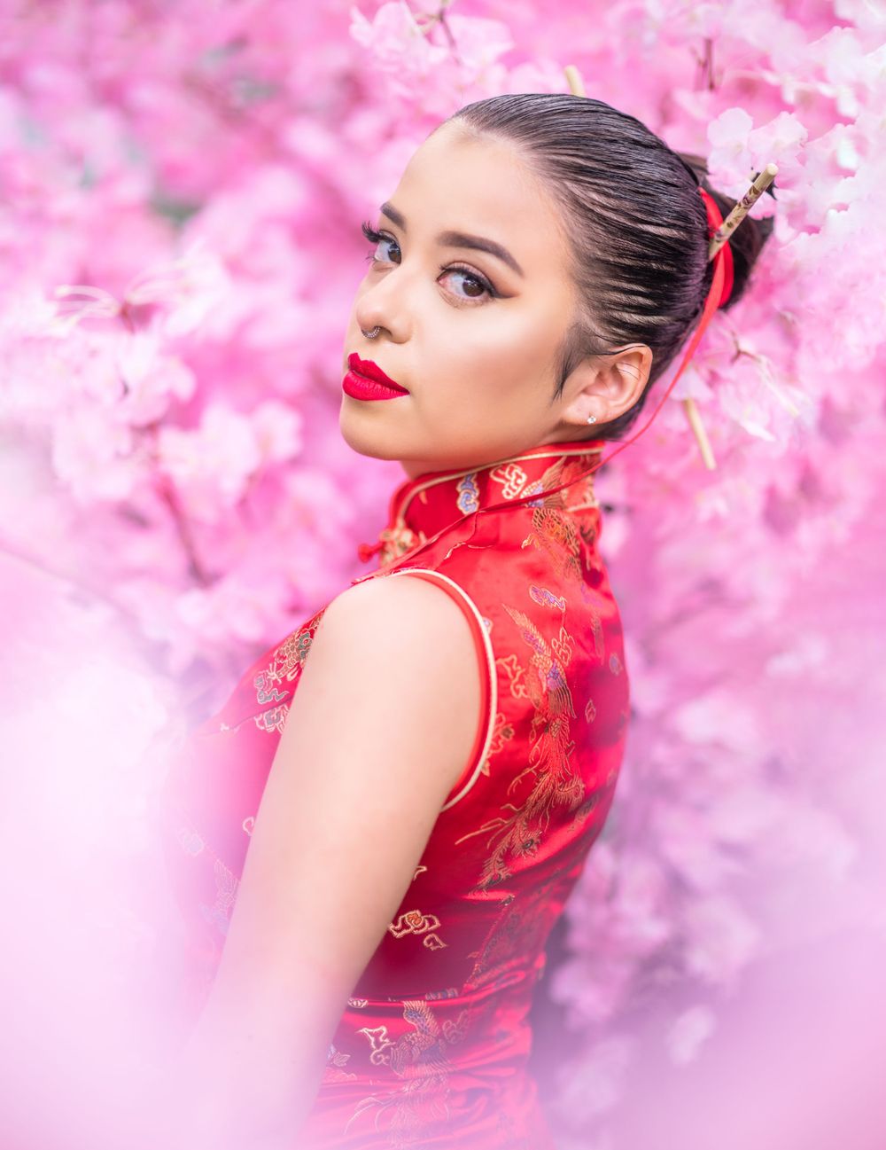 Artistic portrait with red traditional dress against pink cherry blossom backdrop.