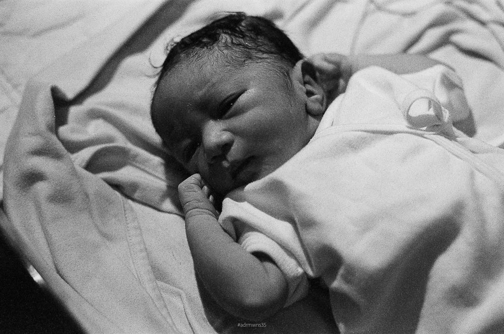 A newborn infant swaddled in white blankets sleeps peacefully in black and white photography.