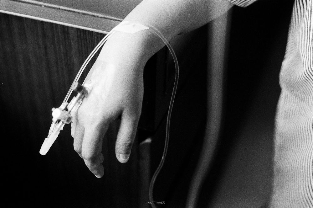 Black and white close-up of a hand holding a medical IV tube against a dark background.