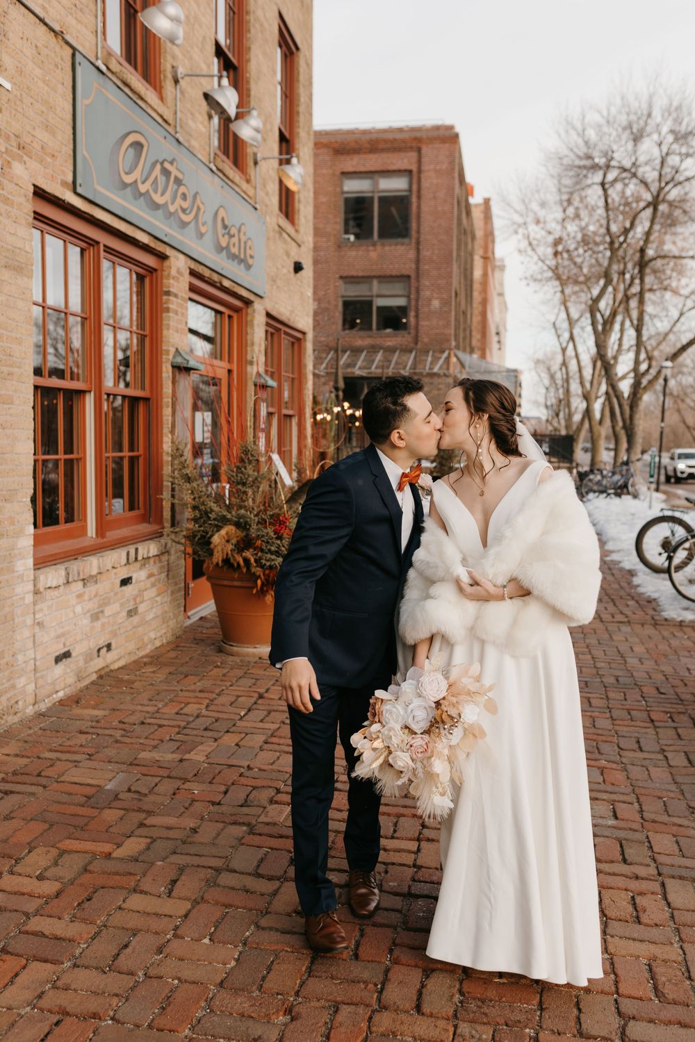 Couple shares a kiss outside Aster Cafe on a snowy winter wedding day on brick sidewalk.