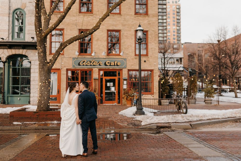 Bride and groom share a tender kiss outside a charming brick cafe on a snowy winter day.
