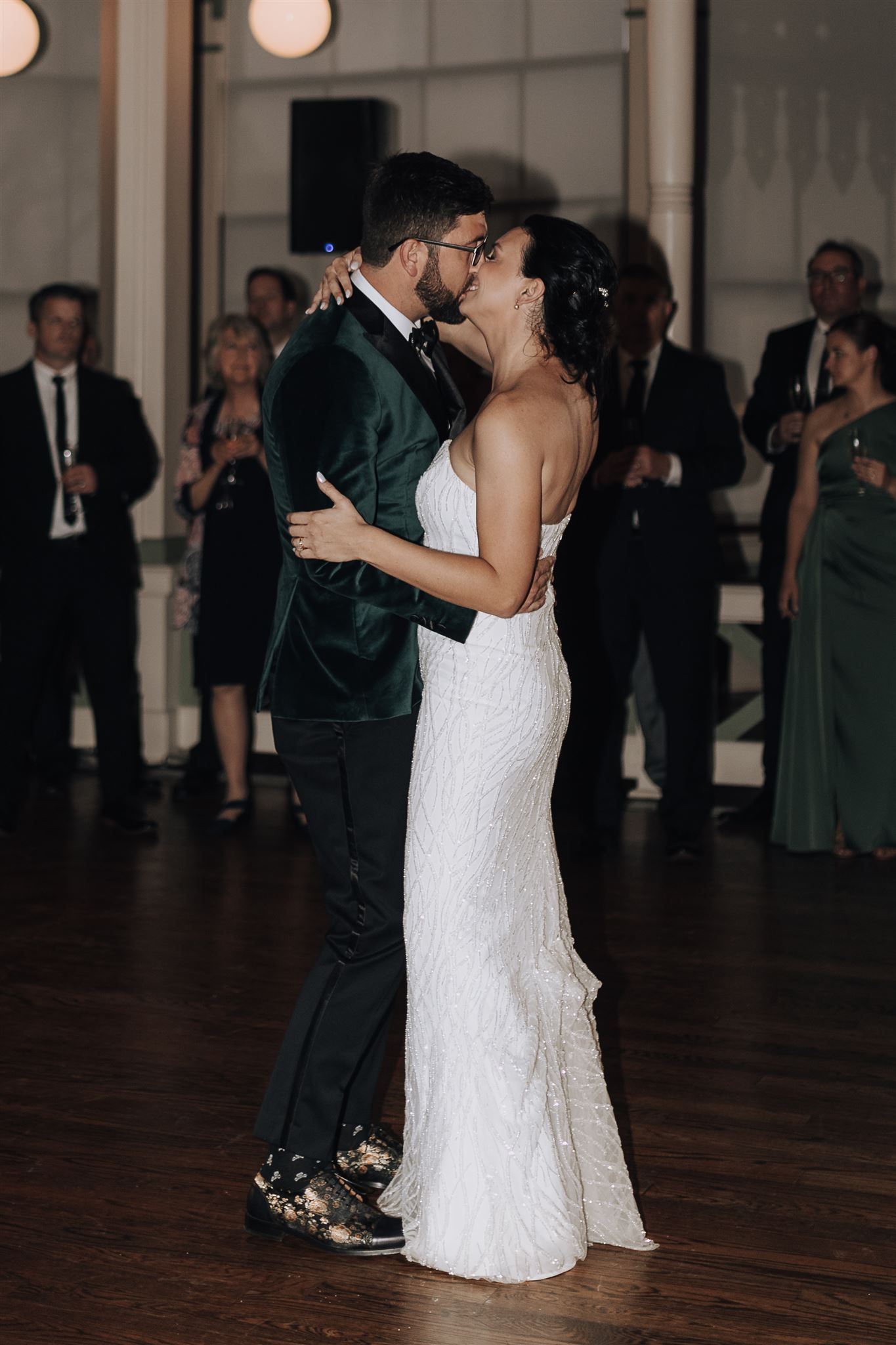 Couple dancing close together during wedding reception with guests watching in background.