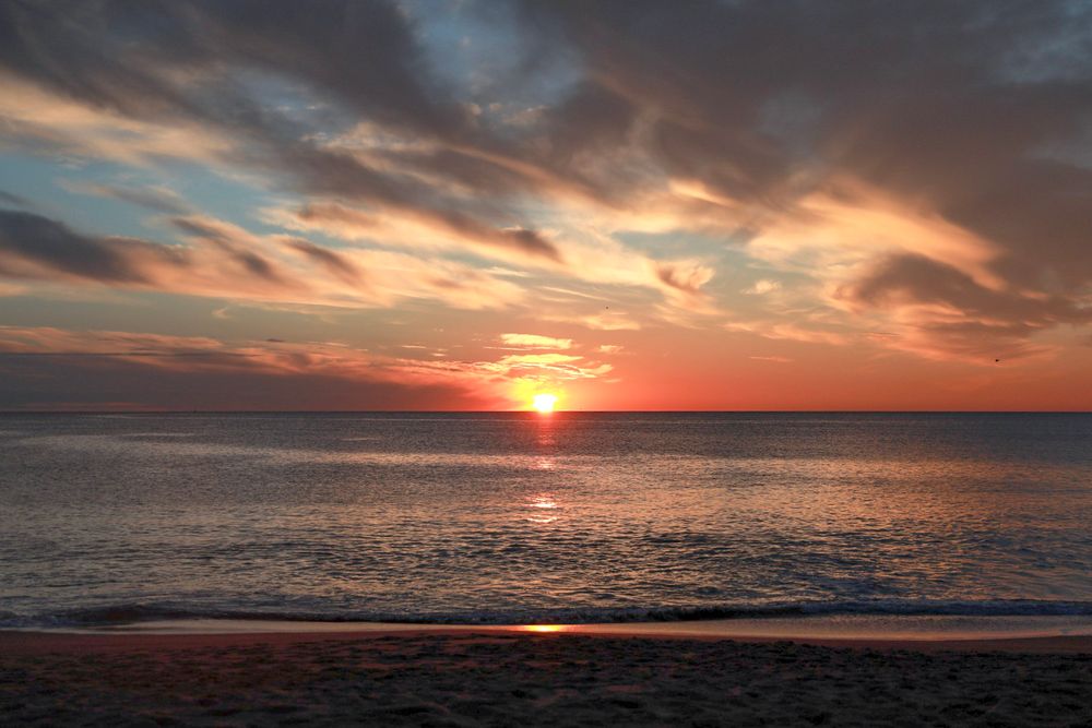 Dramatic clouds light up with orange and pink hues over a serene ocean sunset.