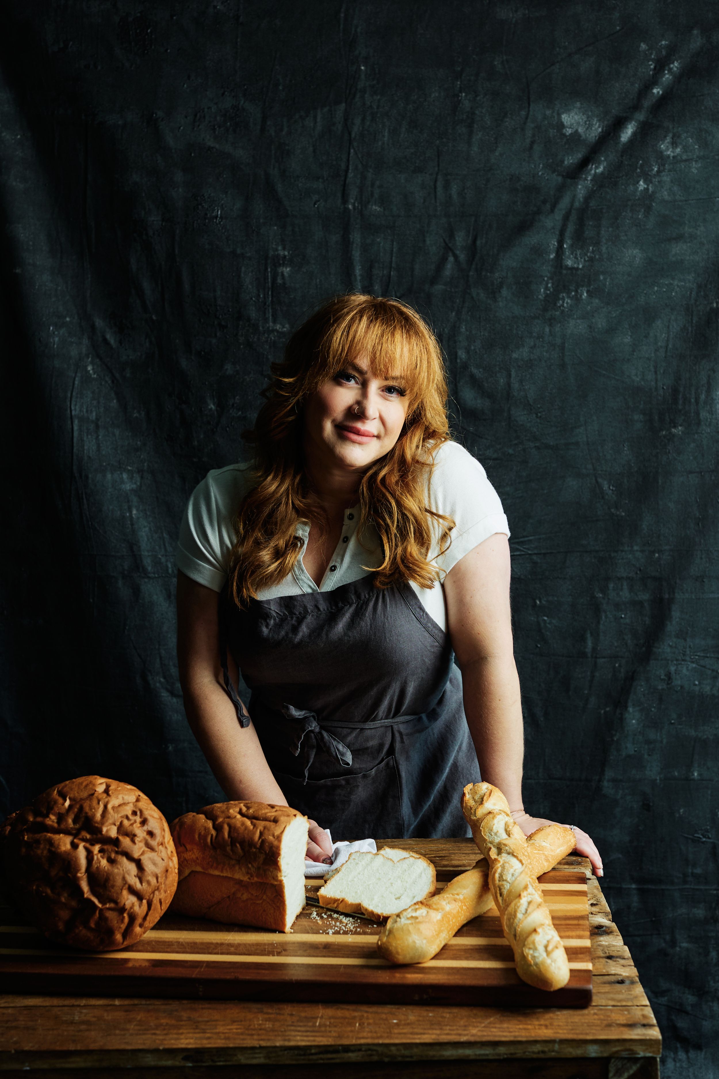 Dark moody food photography with fresh bread loaves on wooden cutting board.