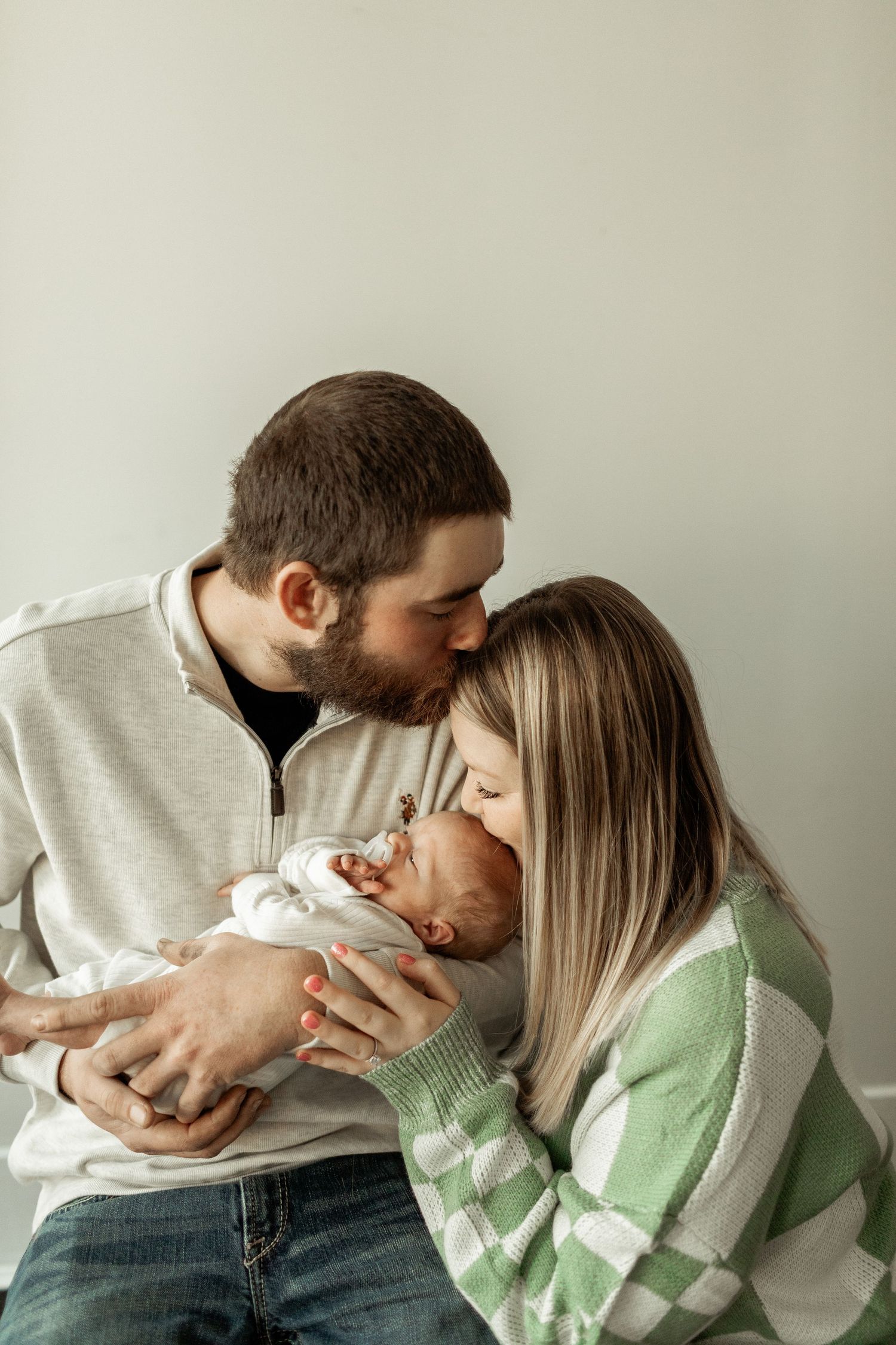 Intimate family moment showing parents embracing their newborn baby in cozy sweaters.