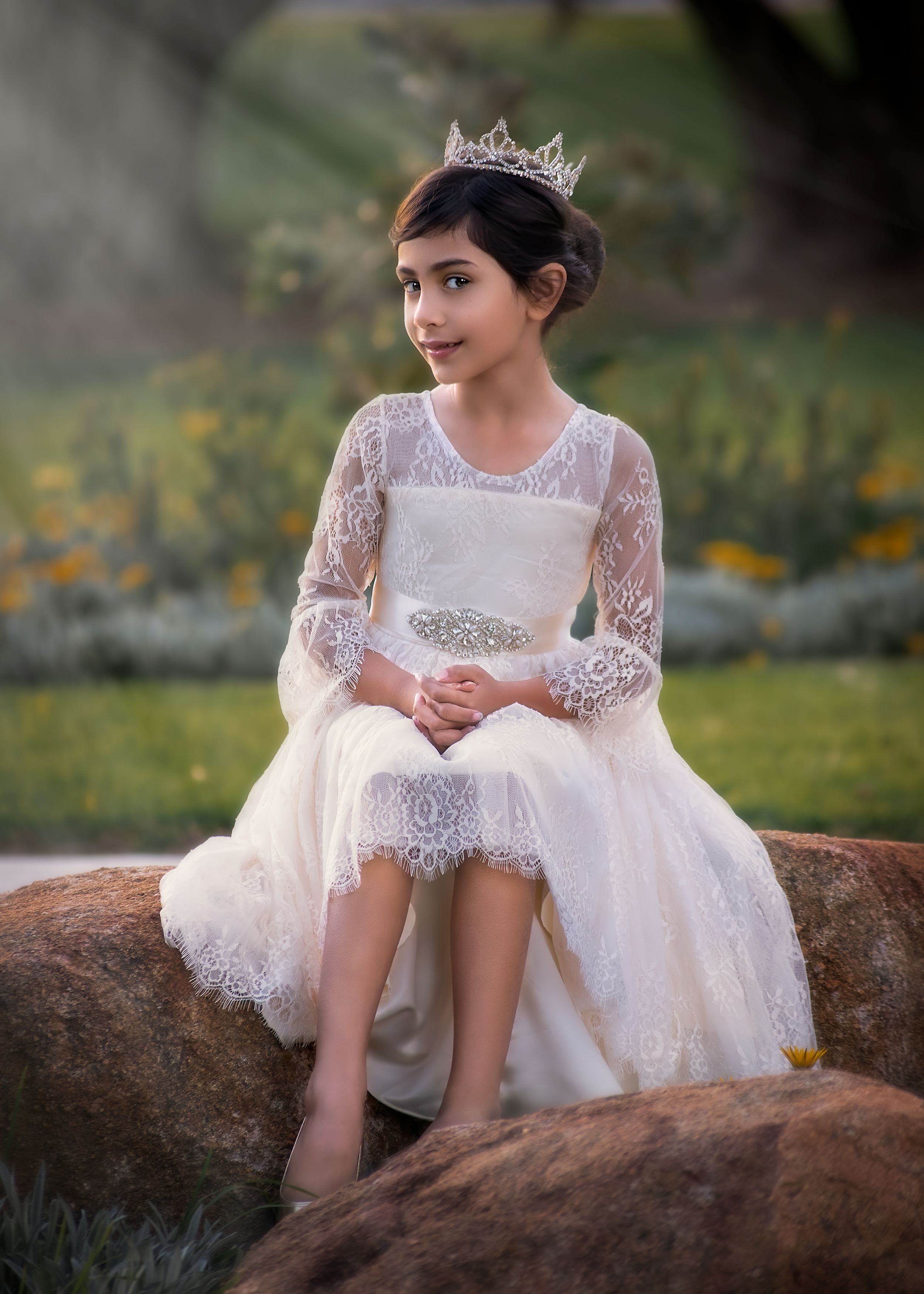 Child Portrait at Don Cuthbertson Reserve. Girl is wearing a crown and cream lace high low gown sitting on a boulder.