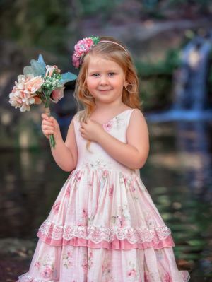 Small girl child in a pink floral gown smiling and holding flowers in front of waterfall at John Oldham Park Perth.