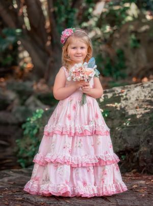 Small girl child in a pink floral gown smiling and holding flowers in front of waterfall at John Oldham Park.
