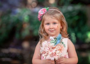 Portrait of a small child wearing a floral headpiece and holding a bouquet of flowers under her chin at John Oldham Park