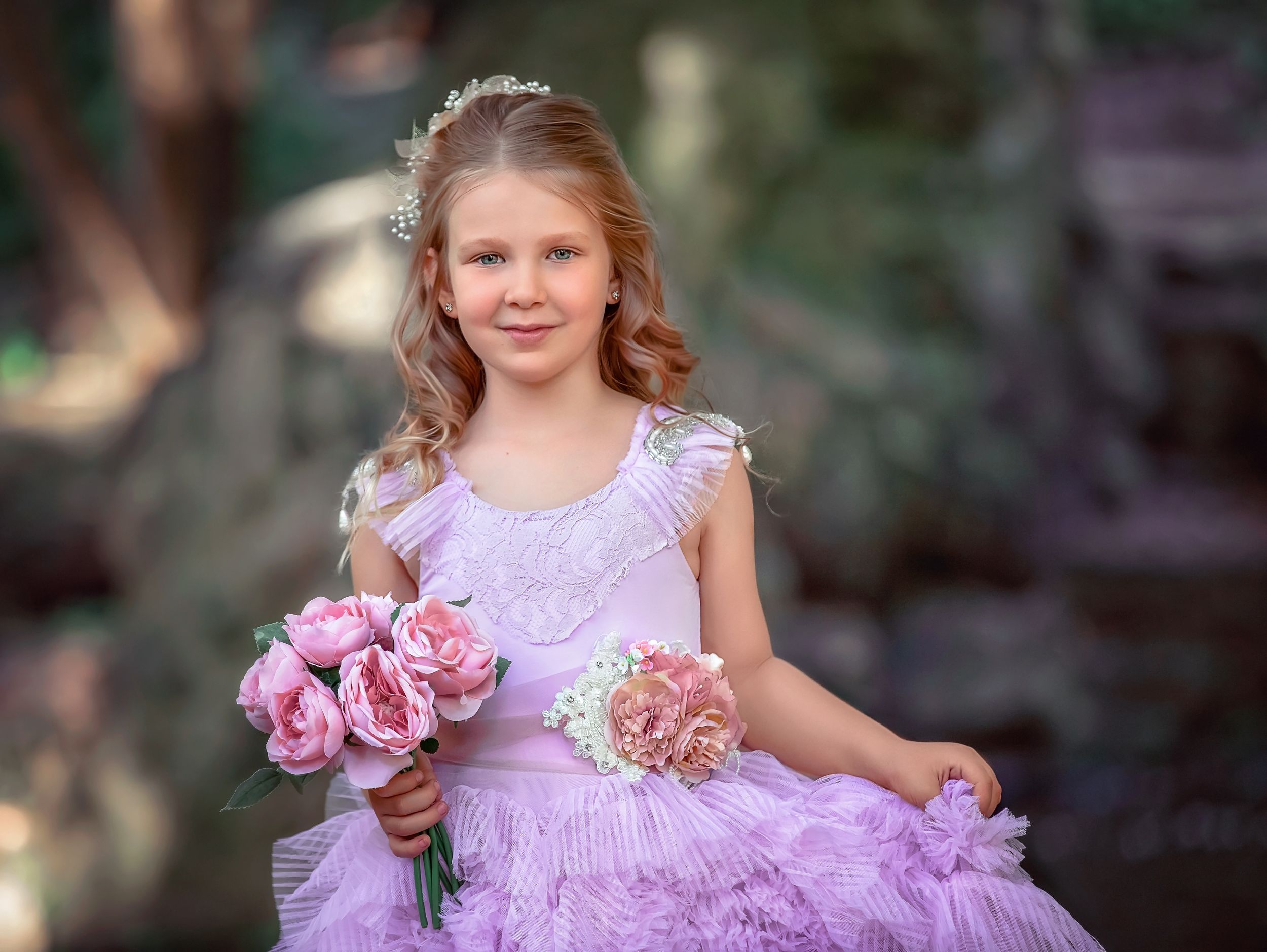 Young girl in a purple ruffle gown holding flowers and smiling.